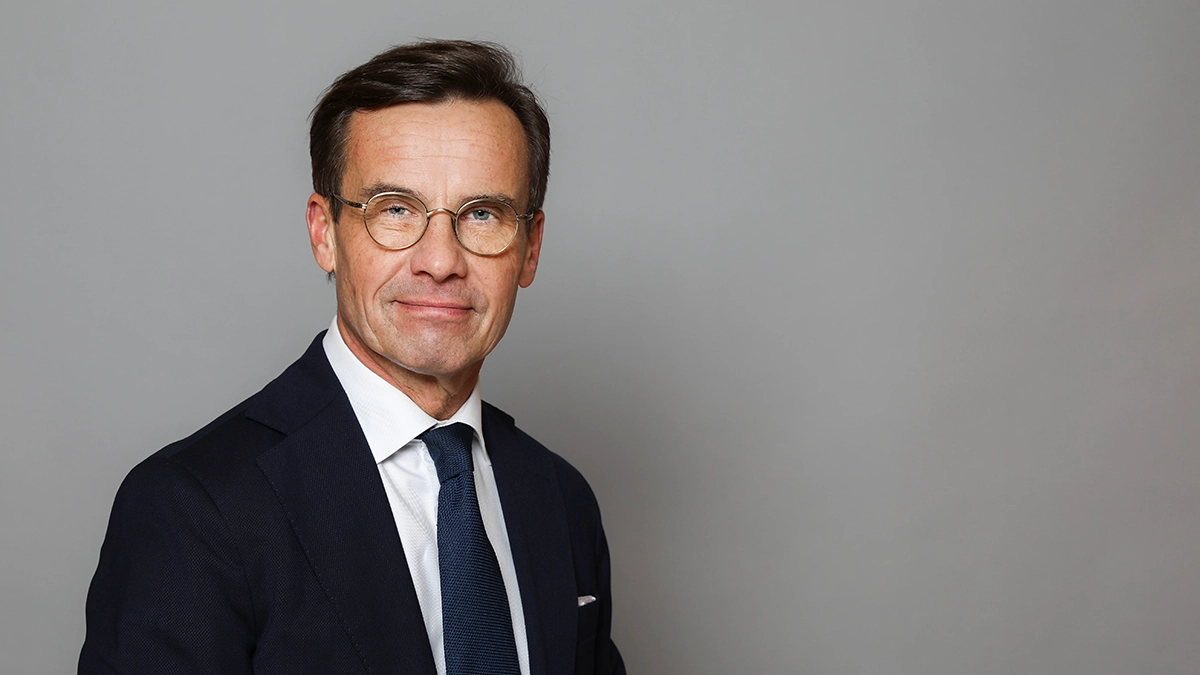 Ulf Kristersson in a black suit and tie, standing against a grey background. He is the Swedish Prime Minister on the date indicated below: 01-04-2024.
